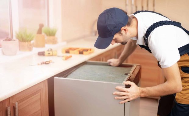 Appliance repair technician pulling a dishwasher out from underneath the kitchen counter for repairs