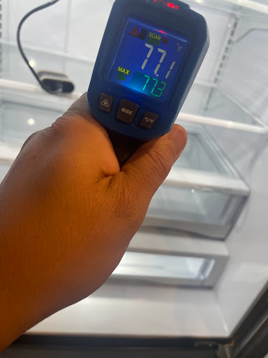 Appliance repair technician using thermometer to gauge refrigerator temperature