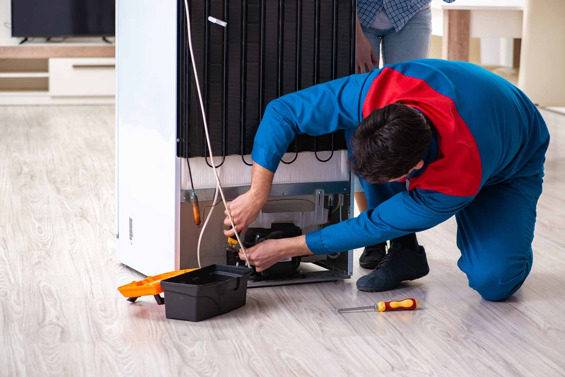 Appliance repair technician kneeling to work on a refrigerator